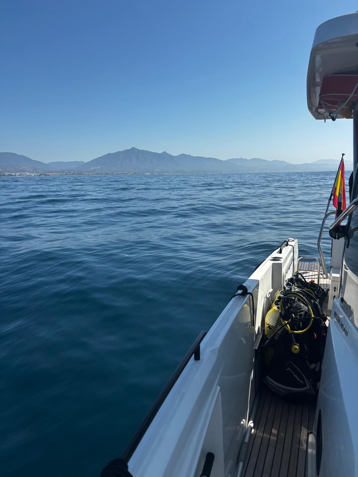 A diver gearing up on deck before a dive with Visitar Marbella, La Concha mountain and the Marbella coast behind